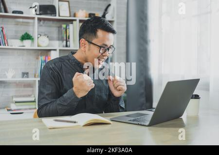 Homme d'affaires asiatique freelance porter des lunettes sourire et heureux de succès tout en travaillant en ligne sur ordinateur portable et de célébrer à la maison ou n'importe où. En fonctionnement Banque D'Images