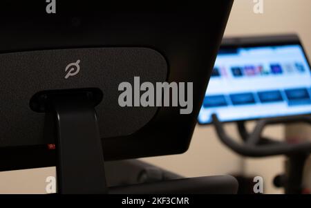 Le logo Peloton est visible à l'arrière d'un tapis roulant Peloton, tandis que l'écran avant d'un Peloton Bike+ est visible en arrière-plan, situé dans une maison. Banque D'Images
