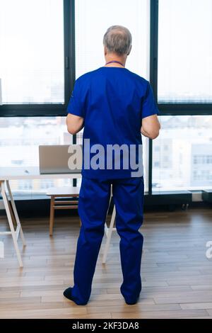 Portrait vertical d'un adulte adulte adulte adulte mature et non reconnaissable, en uniforme médical, debout dans le bureau de l'hôpital sur le fond de la fenêtre. Banque D'Images