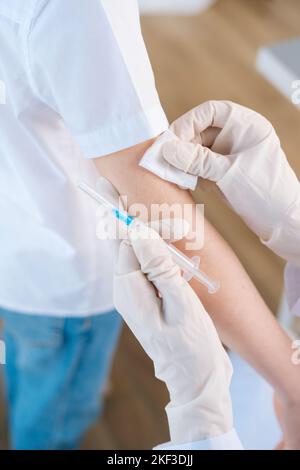 Gros plan vertical dose courte de femme médecin méconnaissable appliquant du plâtre sur l'épaule d'un enfant garçon après l'injection de la vaccination. Banque D'Images