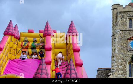 Les enfants jouent sur le grand toboggan gonflable du château médiéval à côté de l'église classée Grade II* du 14th siècle à la Foire de Pinner, juin 2022. Banque D'Images