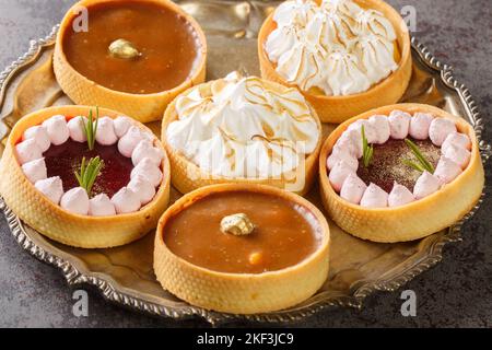 Ensemble de tartelettes de fête avec caillé de meringue et de citron, caillé de framboise, noix et chocolat sur une assiette sur la table. Horizontale Banque D'Images