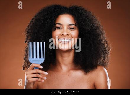 Femme noire, soin des cheveux et sourire en portrait avec peigne, sélection afro ou beauté sur fond marron. Bonne africaine, modèle et femme avec des cosmétiques Banque D'Images