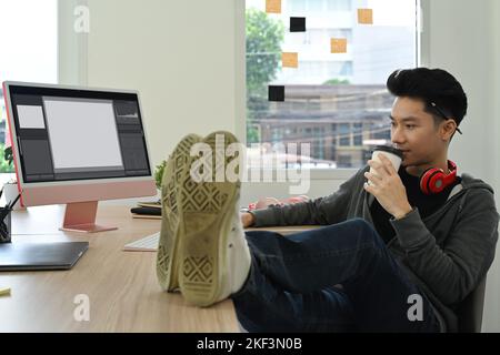 Beau indépendant homme buvant du café et travaillant avec des films et du son dans un studio de bureau créatif Banque D'Images