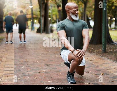Homme noir, fitness et jambe d'étirement dans un parc pour l'exercice d'entraînement ou cardio-training en plein air. L'homme afro-américain est échauffé Banque D'Images