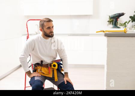 Réparations à domicile. Portrait d'un homme réparateur professionnel avec échelle en métal. Homme souriant dans la combinaison de travail se tient au milieu de la pièce dans laquelle il a Banque D'Images