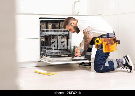 Technicien ou plombier réparant le lave-vaisselle dans un foyer Banque D'Images