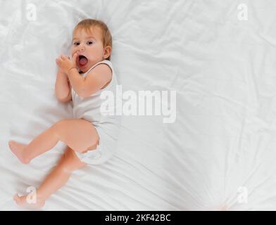 un enfant sur un lit blanc le matin. Textiles et linge de lit pour enfants. Un nouveau-né s'est réveillé ou va se coucher Banque D'Images