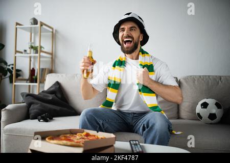 KIEV, UKRAINE - 21 OCTOBRE 2022: Homme stupéfié dans le chapeau de ventilateur tenant une bouteille de bière tout en regardant le championnat, image de stock Banque D'Images