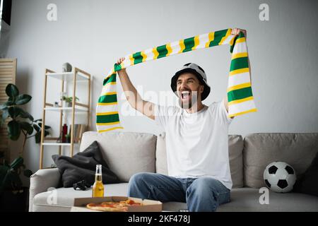 KIEV, UKRAINE - 21 OCTOBRE 2022: Homme étonné dans le chapeau tenant le foulard tout en regardant le championnat, image de la bourse Banque D'Images