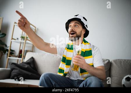 KIEV, UKRAINE - 21 OCTOBRE 2022: Homme stupéfié dans le foulard tenant une bouteille de bière tout en pointant avec le doigt pendant le championnat, image de stock Banque D'Images