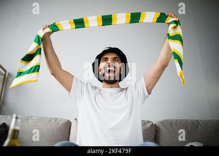 homme excité dans le chapeau de fan tenant le foulard étouffé tout en criant et regardant le championnat, image de stock Banque D'Images