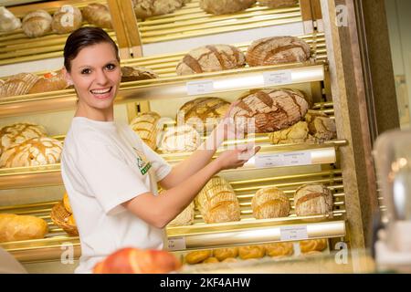 Eine Angestellte in der Bäckerei verkauft frisches Brot, 30, Jahre, dunkelhaarige Verkäuferin, freundlich, lachenend, Banque D'Images