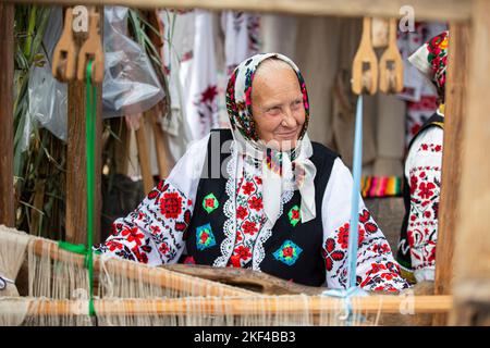 Une vieille femme biélorusse ou ukrainienne dans une chemise brodée à un métier à tisser vintage. Femme âgée slave vêtue de l'ethnie nationale. Banque D'Images