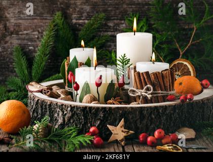 Noël, couronne de l'Avent avec quatre bougies allumées blanches décorées de matériaux naturels. Tranches de pomme fraîche séchée, d'orange et d'épices pour la cuisson. Banque D'Images