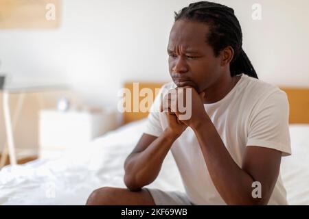 Jeune Africain américain stressé assis sur le lit à la maison Banque D'Images