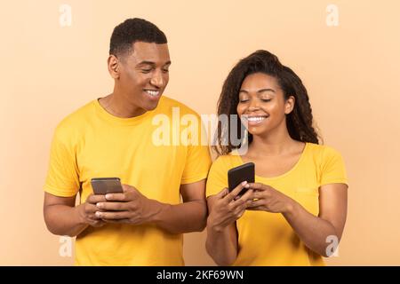 Un jeune couple afro-américain heureux utilisant un smartphone, une dame montrant son gadget à son mari, partageant du contenu sur les réseaux sociaux Banque D'Images