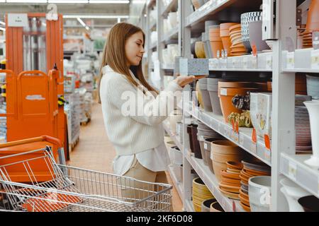 Une femme choisit un pot pour les plantes à la maison dans un magasin de serre, un magasin de quincaillerie, des achats pour la maison et des articles d'intérieur. Banque D'Images