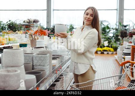 Une femme choisit un pot pour les plantes à la maison dans un magasin de serre, un magasin de quincaillerie, des achats pour la maison et des articles d'intérieur. Banque D'Images