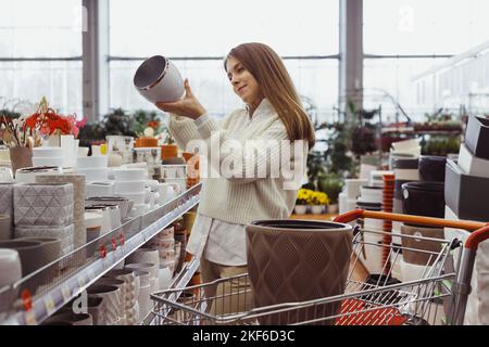 Une femme choisit un pot pour les plantes à la maison dans un magasin de serre, un magasin de quincaillerie, des achats pour la maison et des articles d'intérieur. Banque D'Images
