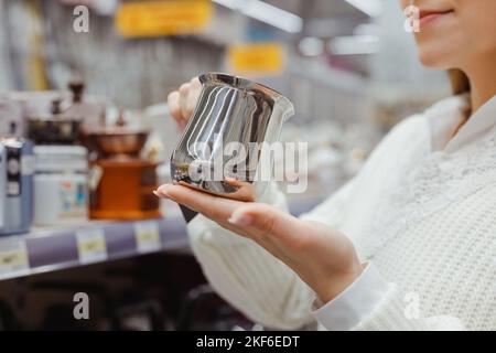 Une jeune femme choisit une cafetière en acier dans le rayon ustensiles de cuisine du supermarché Banque D'Images