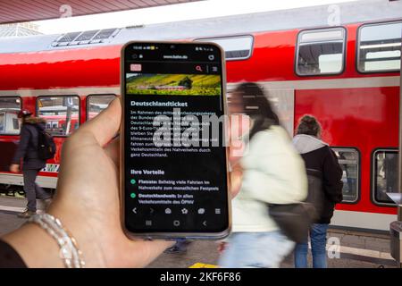 Image symbole Deutschlandticket, billet de 49 euros : gros plan d'un smartphone devant les passagers qui montent et débarquent à un arrêt de train Banque D'Images