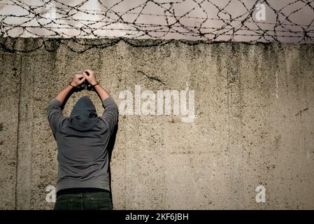 Le criminel se tient devant le mur de la prison avec un fil barbelé. Loi. Menottes. Prison Banque D'Images