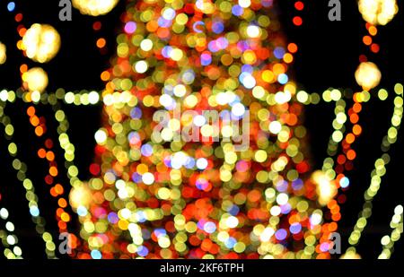 Arrière-plan flou. Belle décoration lumineuse et clignotante du nouvel an et de Noël guirlande et boules brillantes pour arbre de Noël suspendu à l'extérieur à la nuit noire.flou taches de bokeh toile de fond Banque D'Images