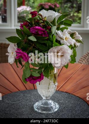 Un bouquet de roses roses roses et blanches dans un vase en cristal sur une table ronde en bois. Banque D'Images