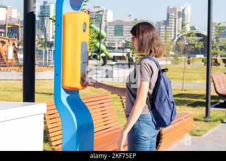 Une jeune fille étudiante avec un sac à dos appuie sur le bouton d'aide du terminal d'urgence sur une rue de ville. La fille demande de l'aide. Bouton SOS Banque D'Images