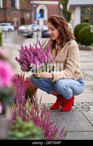 Jeune belle femme tenant un pot avec fleur de la plante de bruyère violette dans un magasin de fleurs de rue. Banque D'Images