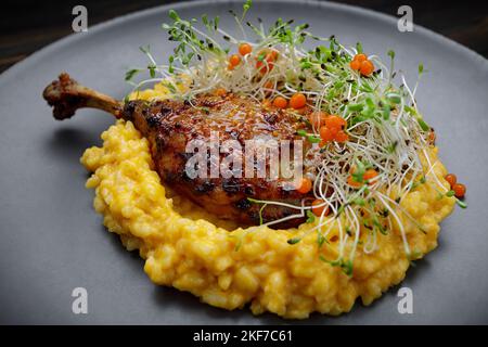 Cuisse de canard avec risotto, potiron et herbes sur fond sombre Banque D'Images