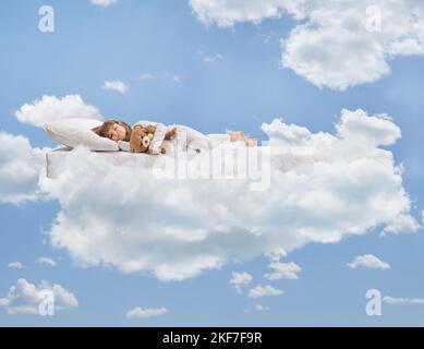 Petite fille en pyjama tenant un ours en peluche et dormant sur des nuages Banque D'Images