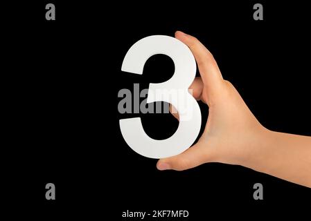 numéro trois à la main, isolé sur fond noir. Numéro trois dans la main d'un enfant sur fond noir. À insérer dans un projet ou une conception. Banque D'Images