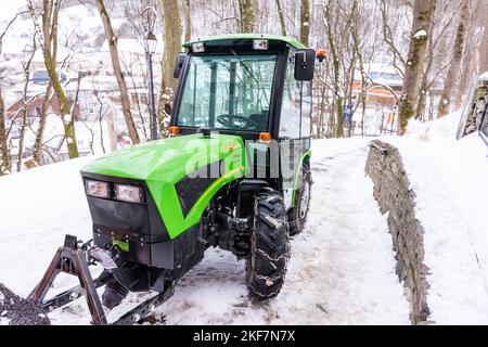 Petit tracteur vert sur une piste enneigée, hiver et gel. Banque D'Images