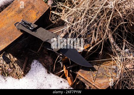 Couteau pliant avec de nombreux outils. Couteau multifonction pour l'armée. Couteau reposant sur du foin et du fer rouillé. Couteau avec attache. Vue de dessus. Banque D'Images