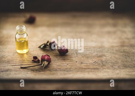 Huile essentielle dans une petite bouteille de verre avec roses séchées dans un bourgeon sur fond de bois. Mise au point sélective et espace de copie pour le texte. Cosmétiques naturels pro Banque D'Images