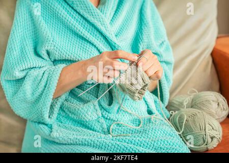 Gros plan des mains des femmes tricoter avec les aiguilles. Détente à la maison, passe-temps, cadeau de laine fait main Banque D'Images