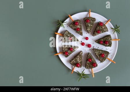 Hors-d'œuvre de Noël sous forme d'arbres de Noël faits de fromage doux et d'herbes d'aneth sèches, décoré de raisins de Corinthe rouges, assiette sur fond vert Banque D'Images