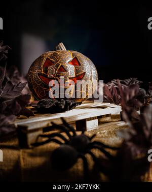 Une verticale de la citrouille sculptée avec une lumière orange foncé entourée de feuilles et d'araignées Banque D'Images