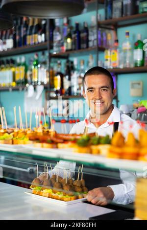 Positif Latin Guy servant des hors-d'œuvre, des tapas, des en-cas sur brochettes au comptoir du bar Banque D'Images