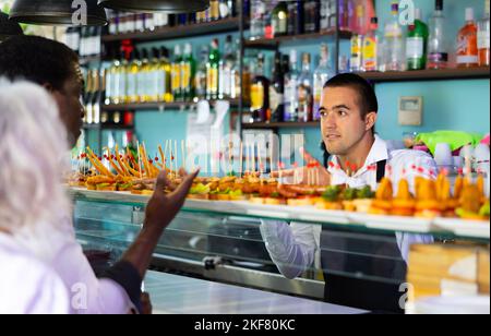 Barman debout au comptoir dans le bar, vendant des sandwiches frais pinchos au client Banque D'Images