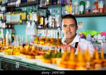 Positif Latin Guy servant des hors-d'œuvre, des tapas, des en-cas sur brochettes au comptoir du bar Banque D'Images