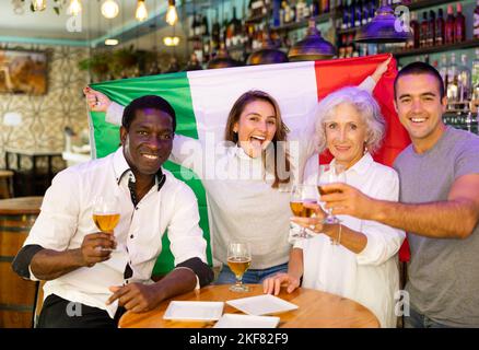 Des supporters de football enthousiastes et variés, drapeau de l'Italie célébrant la victoire avec une pinte de bière au pub Banque D'Images