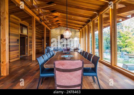 Table à manger en bois avec fauteuils en cuir brut, chaises en cuir noir et éclairage en cuivre de style industriel avec luminaires suspendus en verre dépoli. Banque D'Images