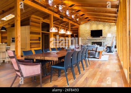 Table à manger en bois avec fauteuils en cuir brut, chaises en cuir noir et éclairage en cuivre de style industriel avec luminaires suspendus en verre dépoli. Banque D'Images