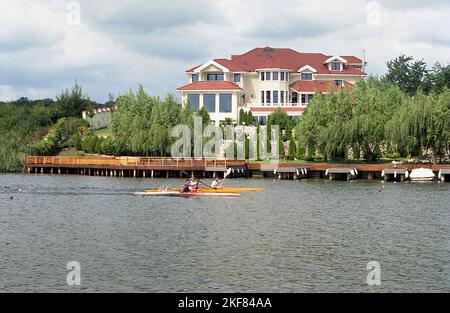 Comté d'Ilfov, Roumanie, environ 2000. Les gens font du kayak sur le lac Snagov, en passant par une grande nouvelle villa résidentielle. Banque D'Images