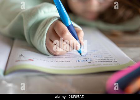 Devoirs.Schoolgirl fait ses devoirs. L'enfant écrit avec un crayon dans un bloc-notes.gros plan crayon dans une main d'enfant.étude et éducation Banque D'Images