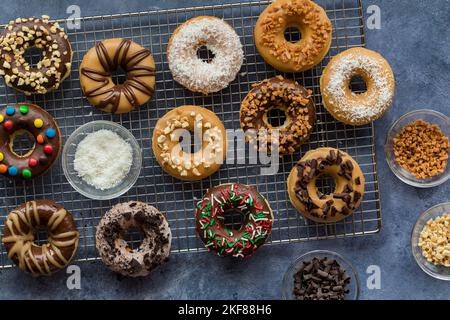 Assortiment de beignets faits maison avec divers glaçures et garnitures, sur une grille de refroidissement. Banque D'Images