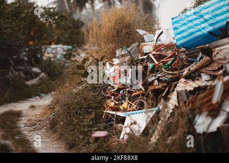 Un dépotoir illégal situé à côté d'une route de terre; une décharge avec beaucoup de feuilles de métal rouillé, de vieilles bicyclettes et d'autres déchets Banque D'Images